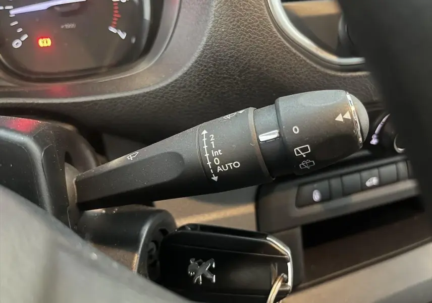 Gros plan sur la manette d'essuie-glace du Peugeot Expert Fourgon blanc, avec tableau de bord et clé visible en arrière-plan.