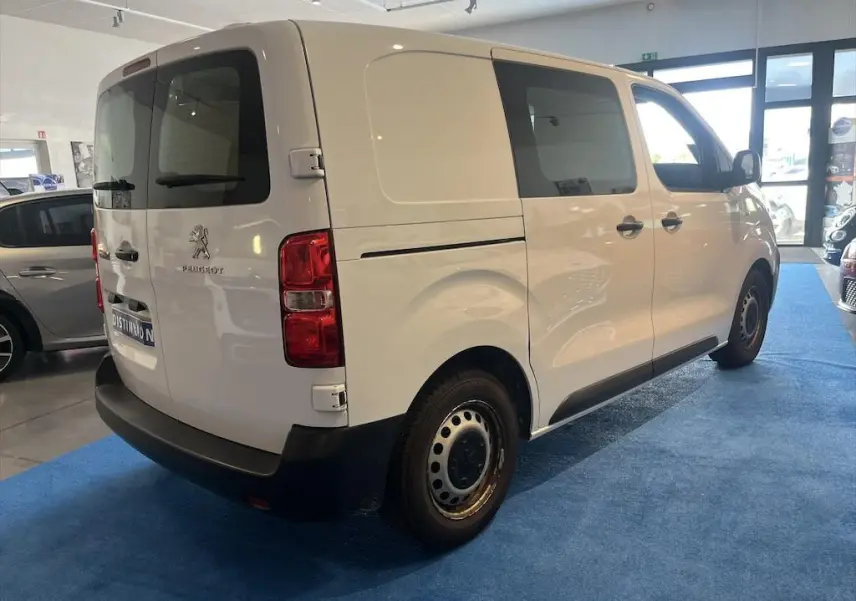 Vue 3/4 arrière droite d'un Peugeot Expert Fourgon blanc stationné en intérieur avec vitres teintées et jantes acier.