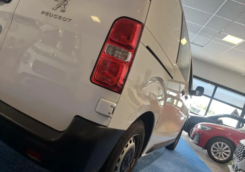 Vue 3/4 arrière droite d'un Peugeot Expert Fourgon blanc dans un showroom avec feux arrière rouges visibles.