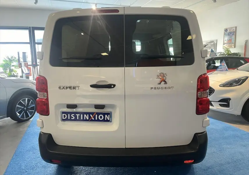 Vue arrière d'un Peugeot Expert Fourgon blanc exposé en showroom avec vitres teintées et logo visible.