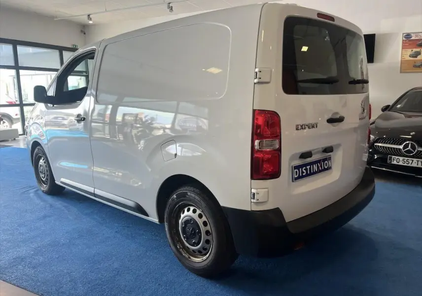 Vue 3/4 arrière droite d'un Peugeot Expert Fourgon blanc exposé en showroom avec plaque Distinxion.