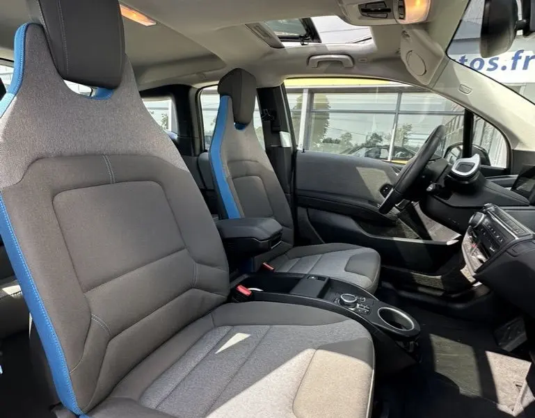 Intérieur de la BMW I3 2022 vue côté conducteur, sièges gris avec surpiqûres bleues et toit ouvrant panoramique.