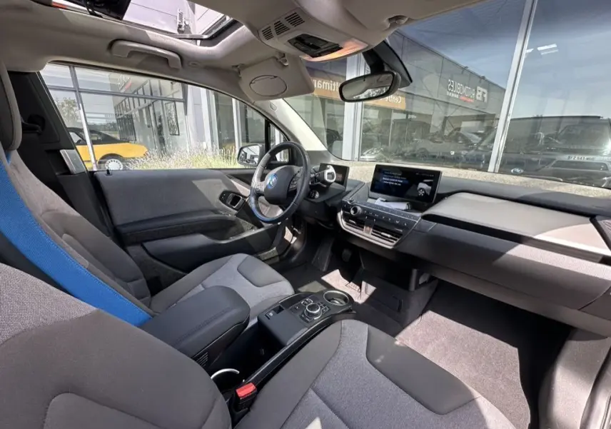 Intérieur avant de la BMW i3 bleue 2022, vue côté conducteur, avec toit ouvrant et tableau de bord moderne.