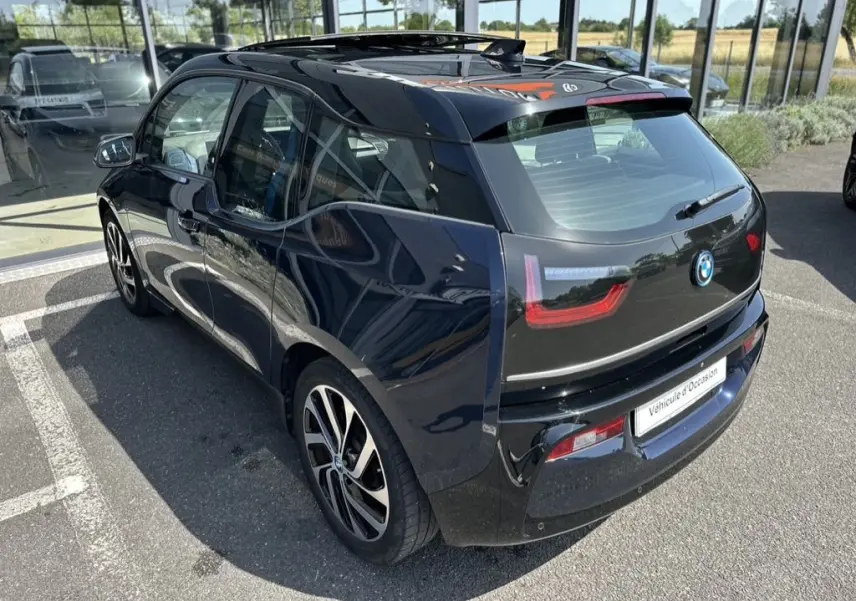 Vue 3/4 arrière droite d'une BMW i3 électrique bleue 2022 avec jantes stylisées et toit vitré en concession.