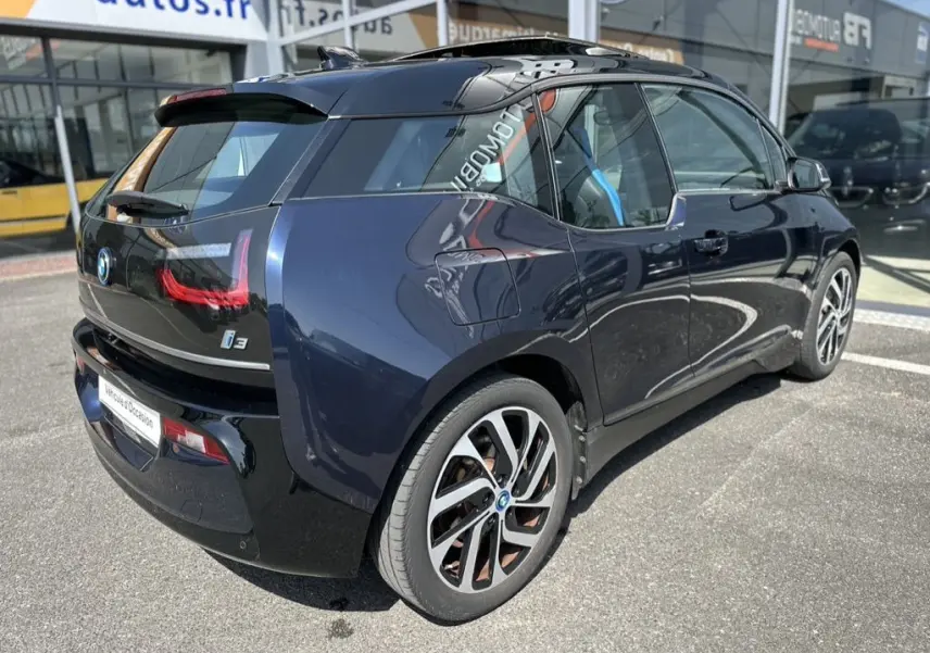 Vue 3/4 arrière droite d'une BMW i3 électrique bleue 2022 avec jantes distinctives et toit noir brillant.