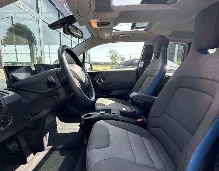 Vue intérieure côté conducteur de la BMW i3 2022 avec sièges gris et bleu et toit ouvrant panoramique.