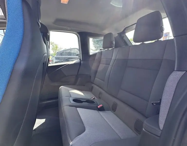 Vue intérieure arrière droite de la BMW i3 120 AH Edition Windmill avec sièges gris et bleu, lumière naturelle entrant par la fenêtre.