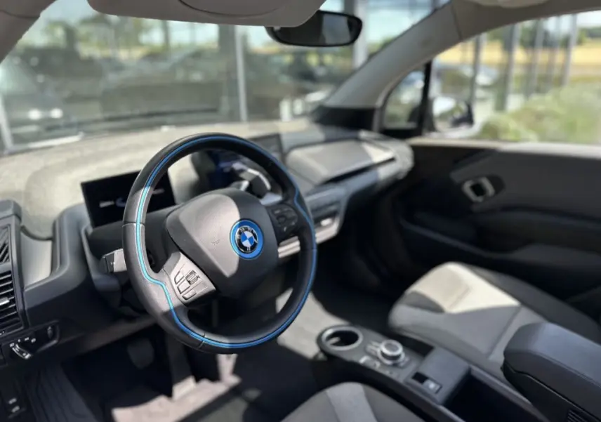 Intérieur de la BMW i3 2022 bleu, vue côté conducteur sur le volant avec surpiqûres bleues et tableau de bord moderne.