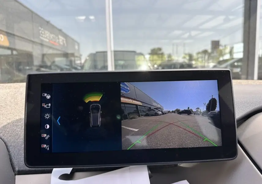 Écran de caméra de recul et capteurs de stationnement dans une BMW i3 bleue, vue intérieure du tableau de bord.