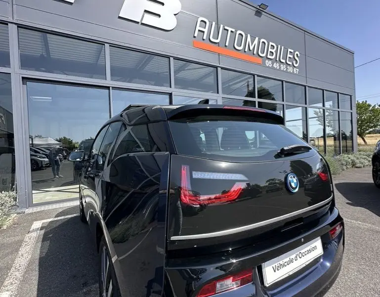 Vue 3/4 arrière d'une BMW i3 noire stationnée devant une concession FB Automobiles par temps clair.