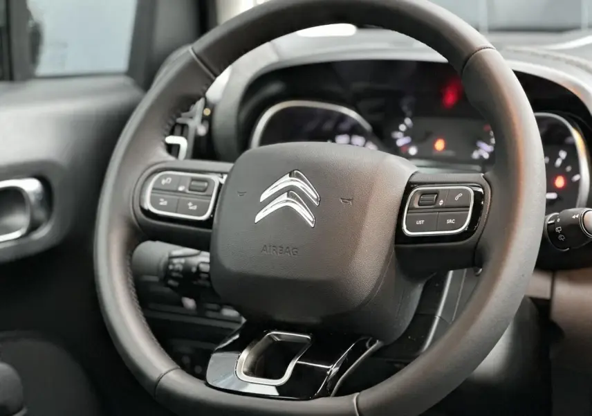 Volant en croûte de cuir noir avec commandes intégrées, tableau de bord flou en arrière-plan d'une Citroën C3 Aircross 2024.