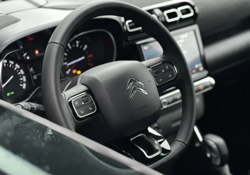 Vue rapprochée du volant noir de la Citroën C3 Aircross 2024 avec commandes intégrées et tableau de bord en arrière-plan.