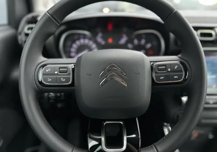 Volant en croûte de cuir noir de Citroën C3 Aircross 2024 avec commandes audio intégrées et tableau de bord flou.