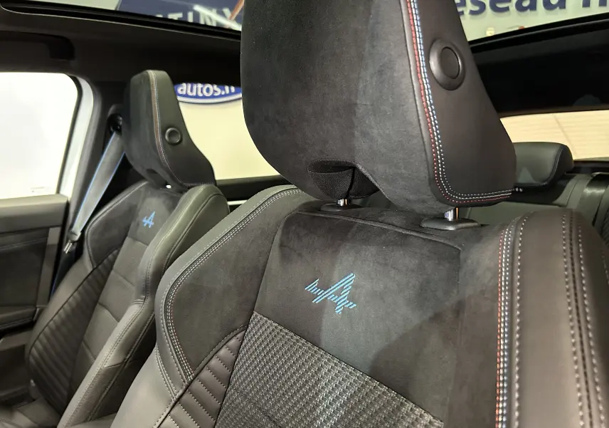 Gros plan sur les sièges avant en cuir et alcantara noirs avec logo Alpine bleu et surpiqûres tricolores visibles.