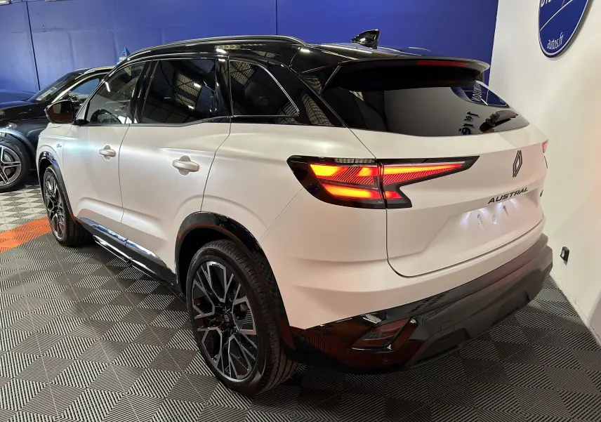 Vue 3/4 arrière droite du Renault Austral blanc nacré satin avec toit noir et feux arrière allumés dans un showroom.