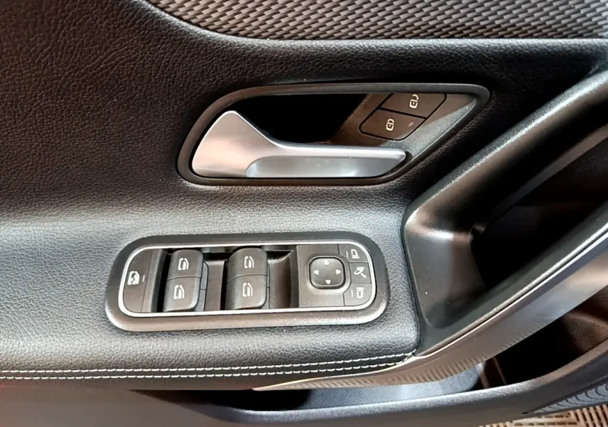 Gros plan sur la porte côté gauche d’une Mercedes CLA 180 d blanche, montrant la poignée alu et les commandes des vitres.