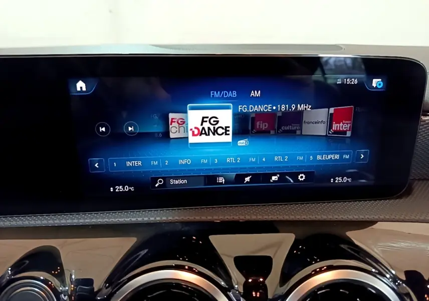 Vue rapprochée de l’écran tactile multimédia et des aérateurs ronds noirs du tableau de bord d’une Mercedes CLA blanche.