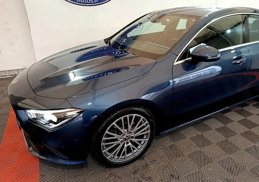 Vue 3/4 avant droit d'une Mercedes Classe CLA bleu métallisé avec jantes alliage multi-branches et phares LED allumés.