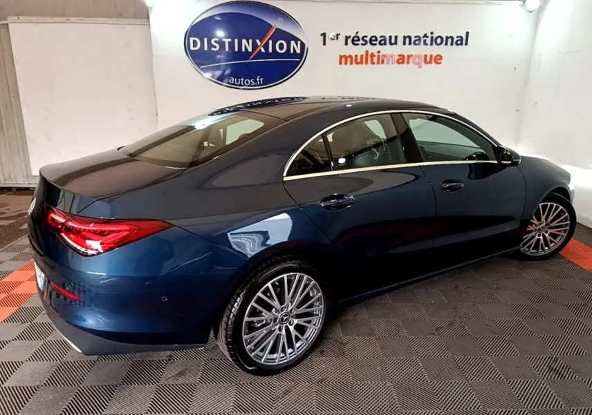 Vue 3/4 arrière droite d'une Mercedes CLA 180 d Business Line bleu foncé avec jantes alliage et feux arrière LED allumés.