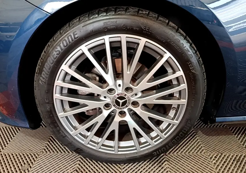Gros plan sur la jante alliage argentée avec logo Mercedes, montée sur un pneu Bridgestone, carrosserie bleu foncé visible.