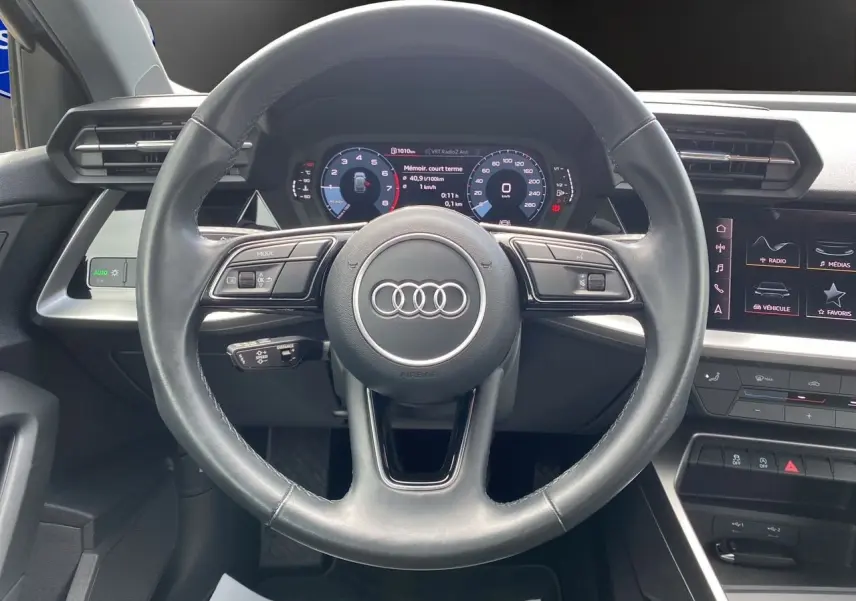 Vue centrée sur le volant noir de l'Audi A3 Sportback 30 TFSI 110 S-Line avec tableau de bord numérique et écran tactile.