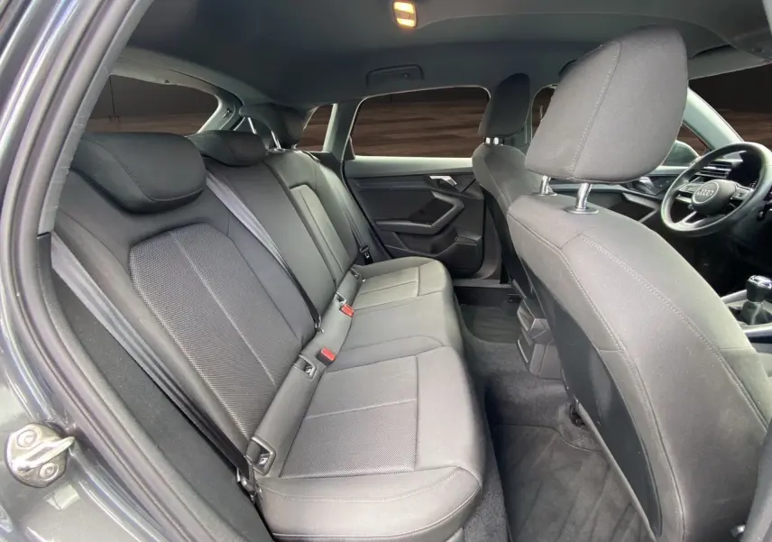 Intérieur arrière de l'Audi A3 Sportback gris Daytona, vue côté gauche avec sièges tissu noir et tableau de bord visible.