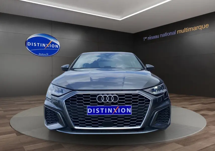 Vue frontale d'une Audi A3 Sportback 30 TFSI S-Line gris Daytona avec calandre hexagonale et phares LED allumés.