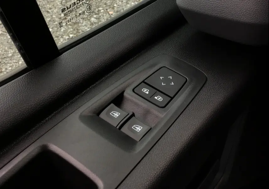 Gros plan sur les commandes de lève-vitres et réglage des rétroviseurs côté conducteur du Renault Master blanc 2025.