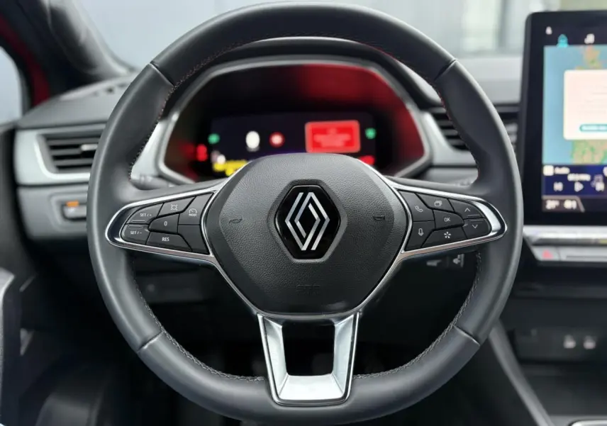 Vue rapprochée du volant noir de la Renault Captur 2025 avec commandes intégrées et tableau de bord numérique flou en arrière-plan.