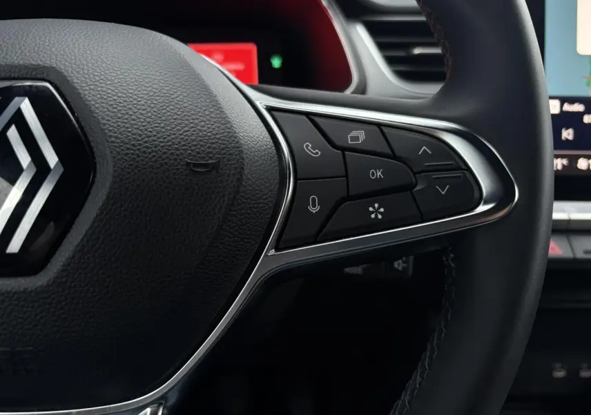 Gros plan sur les commandes à droite du volant noir du Renault Captur 2025 avec logo chromé au centre.