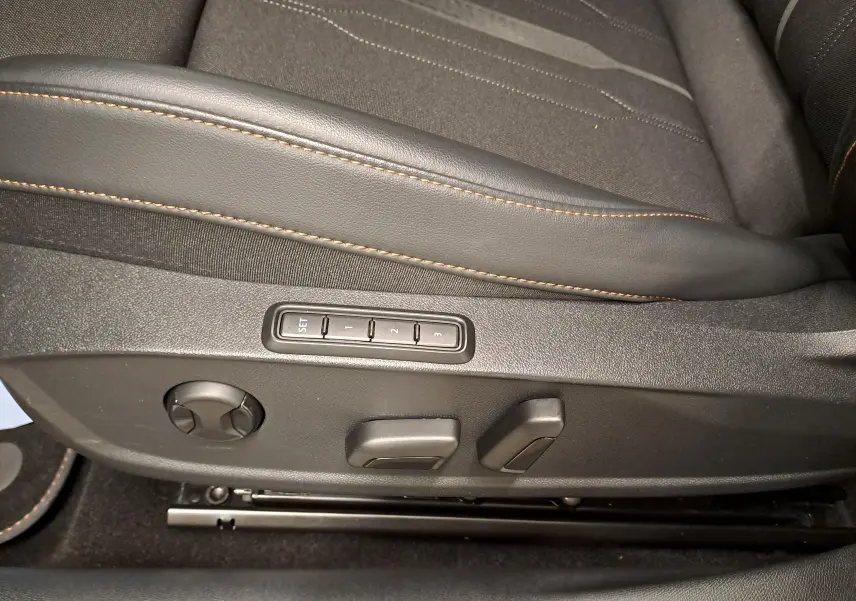 Détail des commandes de réglage électrique du siège conducteur avec surpiqûres orange sur sellerie noire.