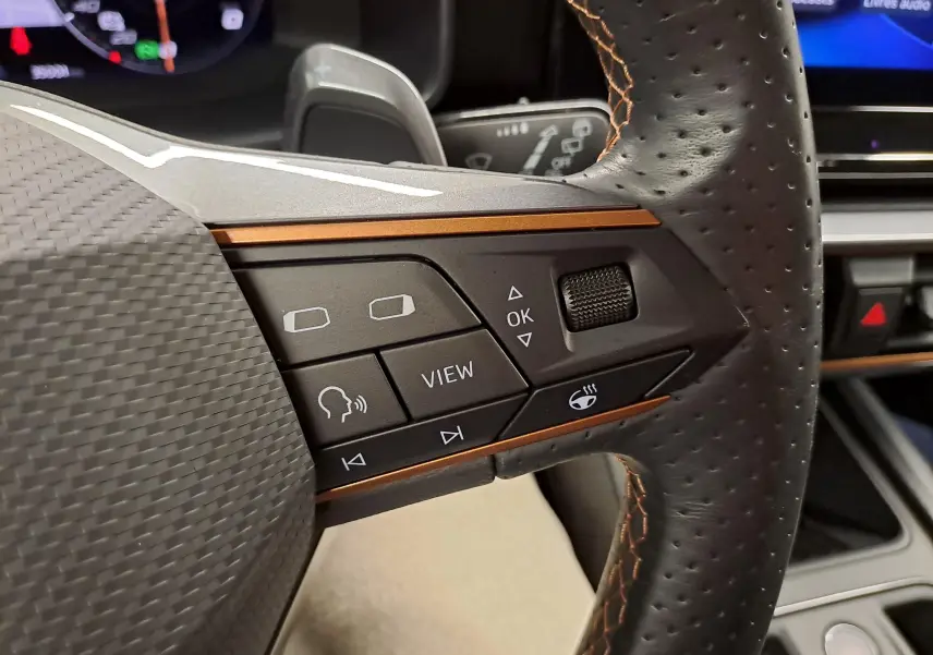 Gros plan sur les commandes à droite du volant perforé avec surpiqûres orange du CUPRA Leon gris magnétique 2023.