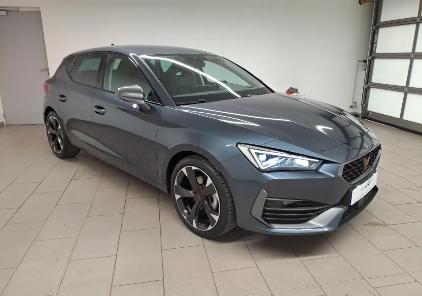 Vue 3/4 avant droite d'une CUPRA Leon 1.5 TSI 150 gris magnétique avec phares LED et jantes noires distinctives.