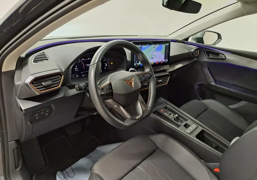 Vue intérieure côté conducteur de la CUPRA Leon 1.5 TSI 2023, avec tableau de bord numérique et éclairage d’ambiance violet.