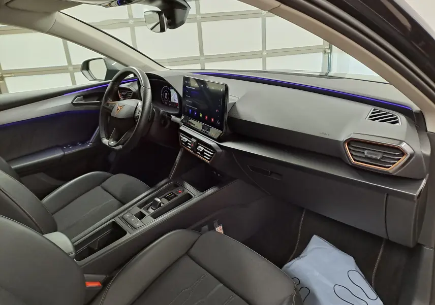 Vue intérieure côté conducteur du CUPRA Leon 1.5 TSI 150 DS7 V 2023, avec tableau de bord moderne et éclairage d’ambiance violet.