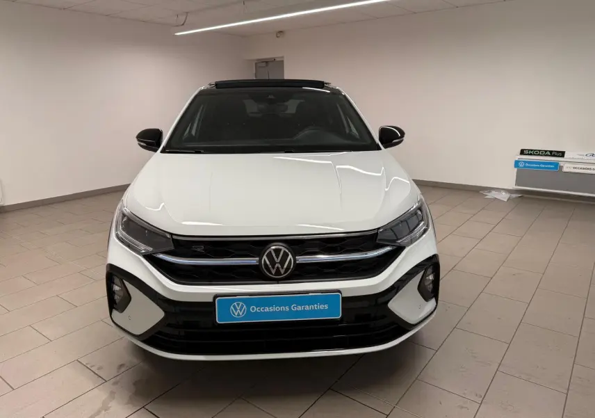 Vue de face d'un Volkswagen Taigo blanc pur avec toit noir, calandre R-Line et éclairage LED dans un showroom.