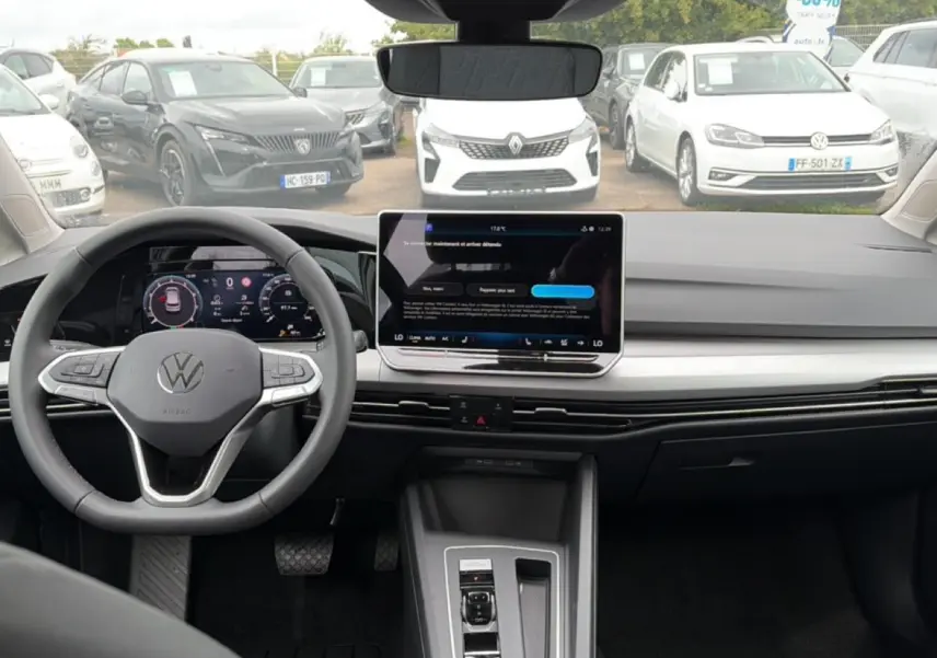 Vue intérieure avant de la Volkswagen Golf 1.5 bleu glacier, avec tableau de bord numérique et écran tactile central.
