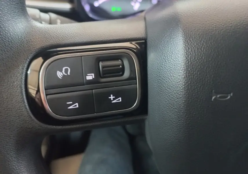 Gros plan sur les commandes multifonctions à gauche du volant noir du Citroën C3 BlueHDi 2024.