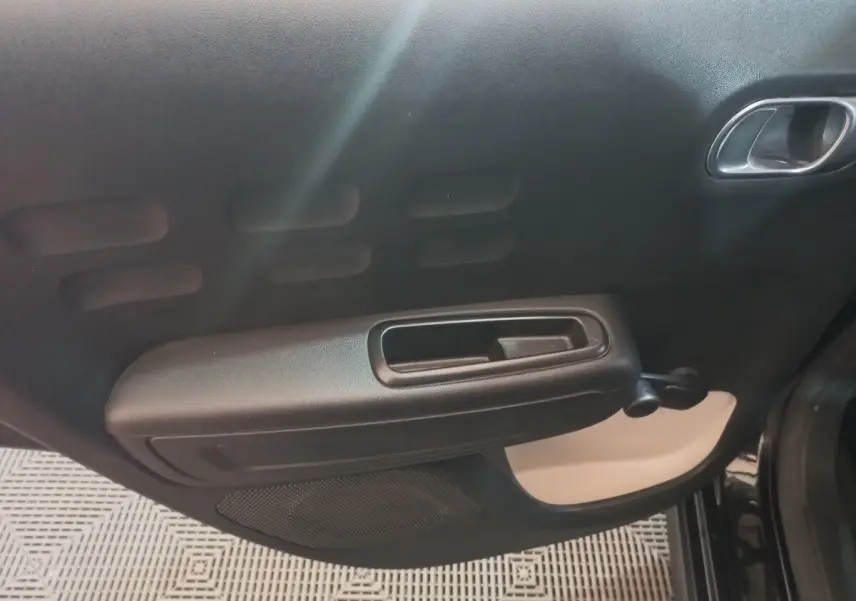 Vue intérieure du panneau de porte arrière gauche noir de la Citroën C3 2024 avec poignée et commande de vitre manuelle.