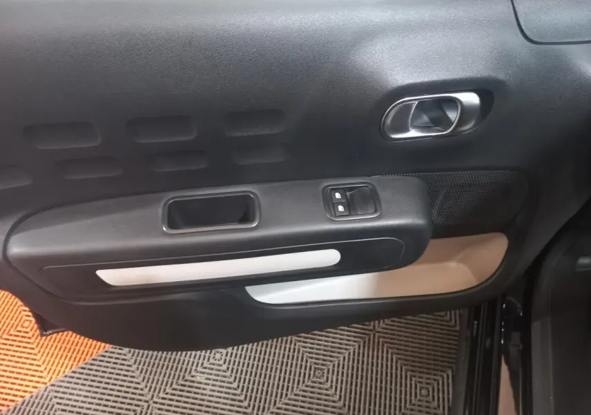 Vue intérieure du panneau de porte avant gauche noir avec poignée argentée et commandes de vitres électriques.