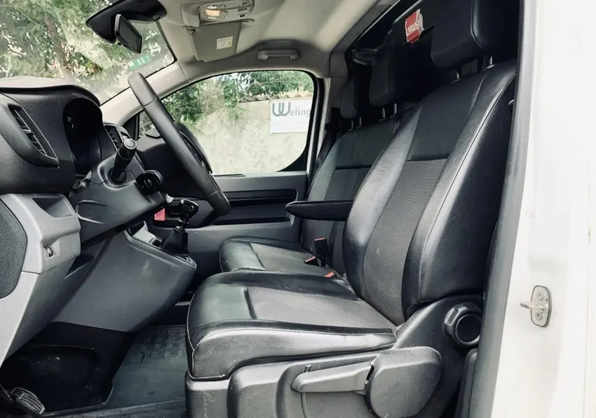 Vue intérieure côté conducteur du Citroën Jumpy blanc 2020, sièges noirs en cuir avec accoudoir et tableau de bord visible.