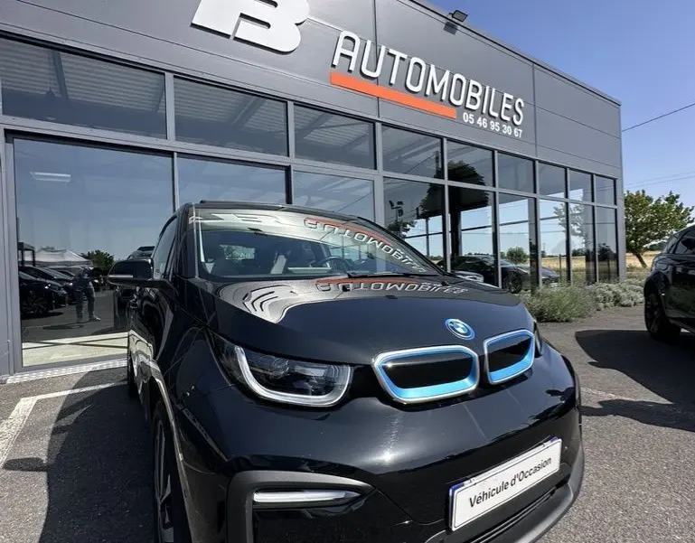 BMW i3 noire vue de face en léger 3/4 avant droit, avec calandre bleue distinctive et plaque "Véhicule d'Occasion" visible.