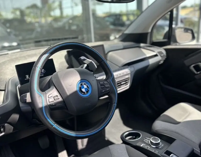 Vue intérieure côté conducteur de la BMW i3 noire 2022, volant avec liseré bleu et tableau de bord moderne.