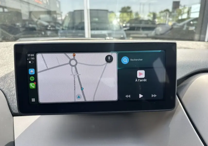 Écran tactile central affichant la navigation et la musique dans une BMW i3 noire, vue intérieure du tableau de bord.