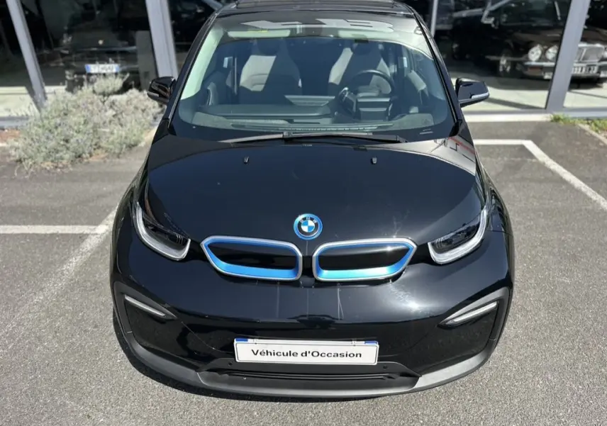 Vue avant plongeante d'une BMW i3 noire électrique avec calandre bleutée et plaque "Véhicule d'Occasion" visible.