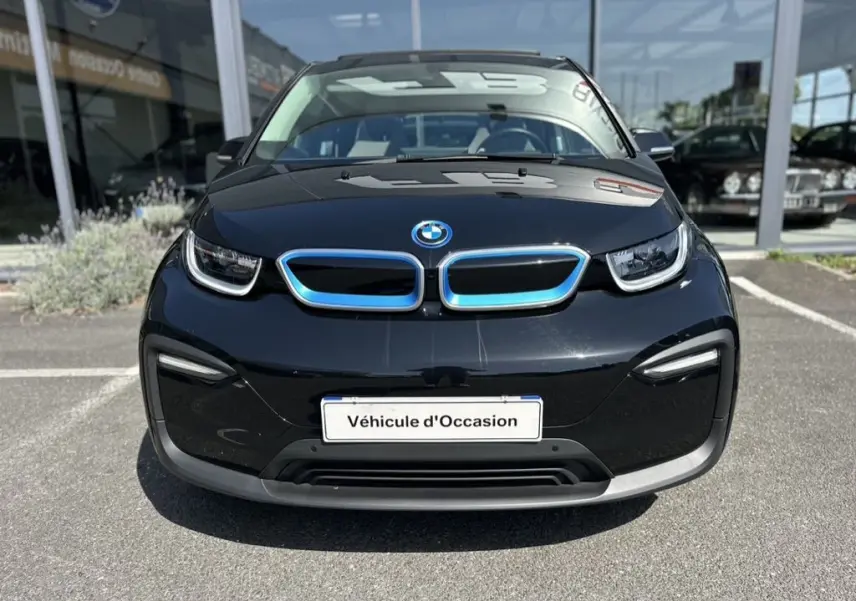 Vue frontale d'une BMW i3 noire 2022 avec calandre bleutée et plaque "Véhicule d'Occasion" en concession.