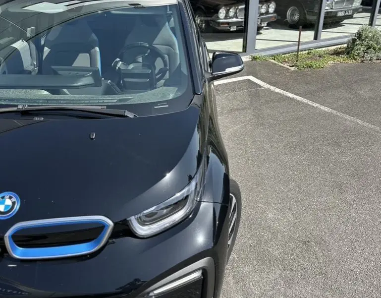Vue 3/4 avant droite d'une BMW i3 noire électrique 2022 avec calandre bleue distinctive, stationnée devant une vitrine.