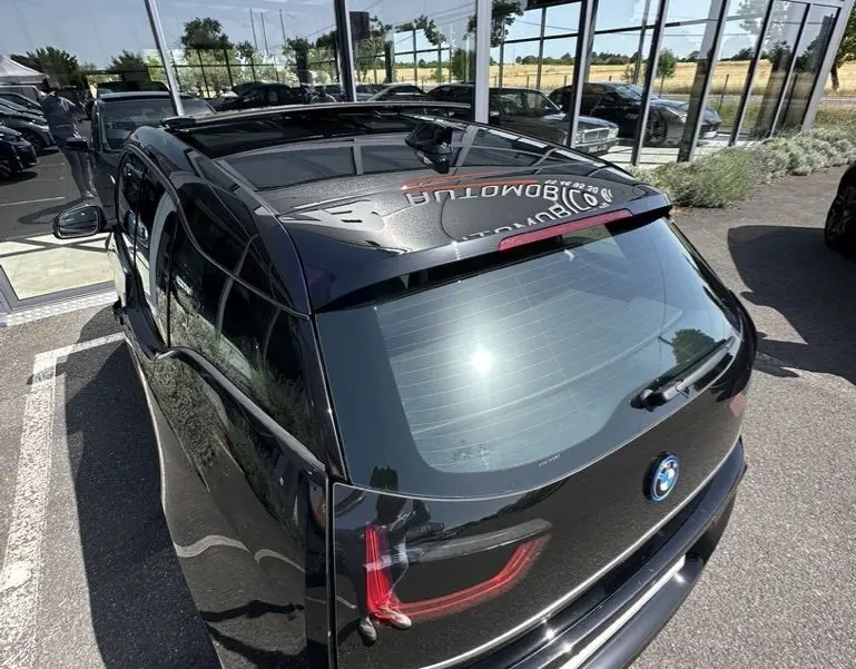 Vue 3/4 arrière d'une BMW i3 noire électrique 2022, avec feux arrière LED et toit panoramique visible.