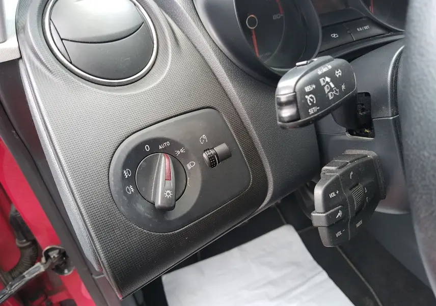 Détail du tableau de bord côté gauche d'une SEAT Ibiza ST rouge, avec commandes d'éclairage et régulateur de vitesse.