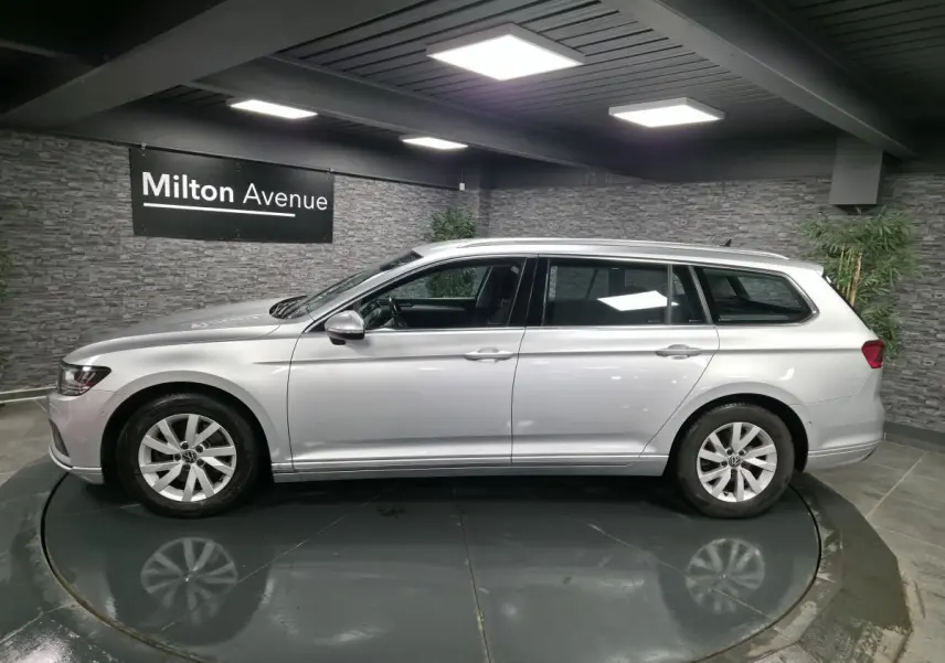 Volkswagen Passat SW gris métallisé vue de profil côté gauche dans un showroom avec mur en pierre grise.